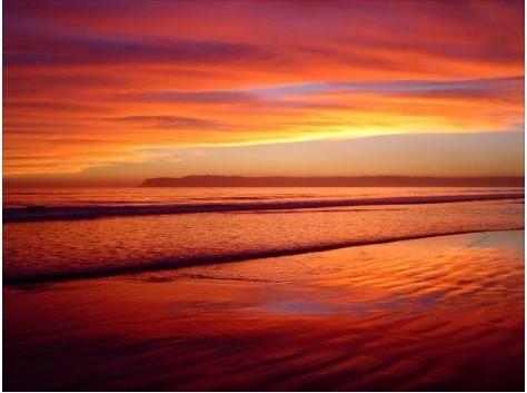 A sunset over the ocean with waves in the foreground.